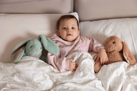 Foto de Lindo niño pequeño con juguete esponjoso conejito en la cama blanca - Imagen libre de derechos