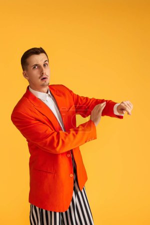 Téléchargez les photos : Joyeux jeune homme drôle en veste orange et pantalon rayé sur fond jaune. - en image libre de droit
