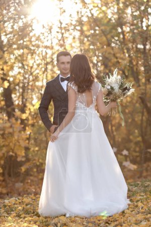 Foto de Hermosa novia en vestido de novia blanco y novio de pie al aire libre sobre fondo natural en el día soleado - Imagen libre de derechos