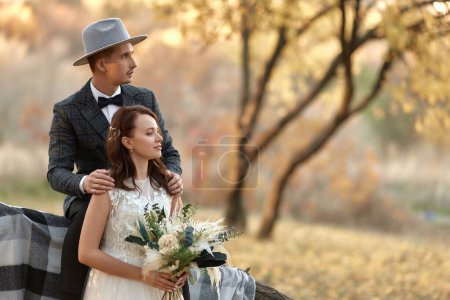 Téléchargez les photos : Belle mariée élégante heureuse et marié dans le chapeau près de l'arbre en automne - en image libre de droit