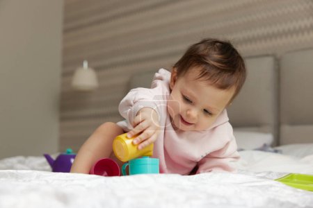 Foto de Feliz linda niña jugando y fingiendo beber té de tazas de juguete en la cama - Imagen libre de derechos