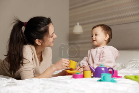 Photo for Beautiful mother and little child daughter playing tea party in bedroom - Royalty Free Image
