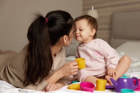 Téléchargez les photos : Mère et petite fille enfant jouant au thé et passant du temps ensemble dans la chambre à coucher, famille s'amusant - en image libre de droit