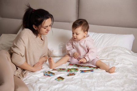 Photo for Pretty mother playing with puzzle pieces with her little child girl in bedroom - Royalty Free Image