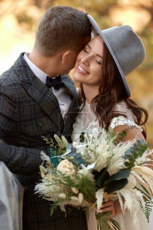 Téléchargez les photos : Belle mariée élégante heureuse en chapeau et marié riant en plein air - en image libre de droit
