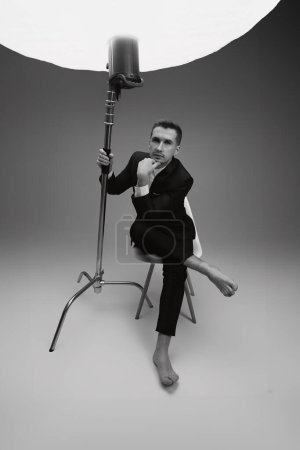 Téléchargez les photos : Élégant modèle homme en costume noir pieds nus en photostudio. noir et blanc - en image libre de droit