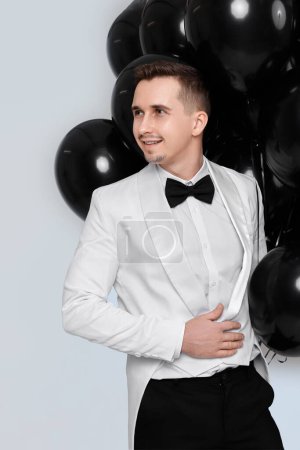 Foto de Elegante hombre sonriente en traje esmoquin blanco con globos de aire negro sobre fondo blanco. Celebración - Imagen libre de derechos