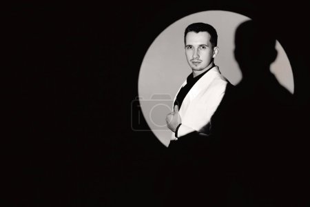 Foto de Elegante hombre en traje blanco esmoquin en el círculo de la luz, espacio de copia. blanco y negro - Imagen libre de derechos