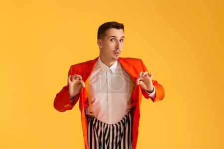 Cheerful funny young man in orange jacket and striped pants on vibrant yellow background.