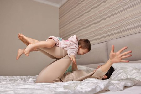 Photo for Happy Caucasian mother lifting in air cute little child daughter in bedroom - Royalty Free Image