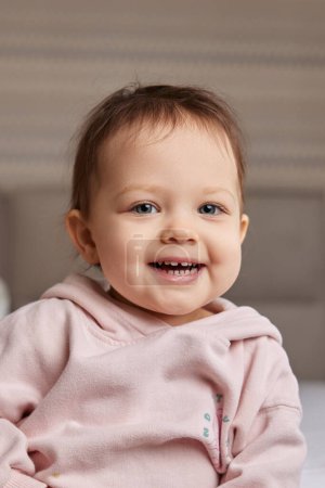 Cute little baby girl smiling in pink shirt in bedroom