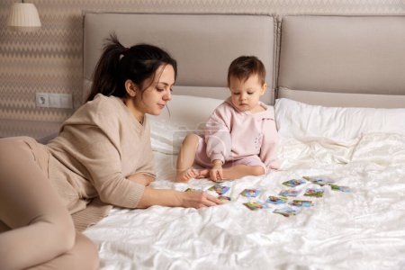 Photo for Pretty mother playing puzzle together with her little child girl in bedroom - Royalty Free Image