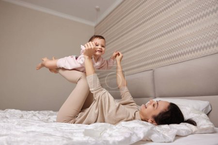 Glücklich kaukasische Mutter heben in der Luft niedlich kleines Kind Mädchen und spielen zusammen im Schlafzimmer