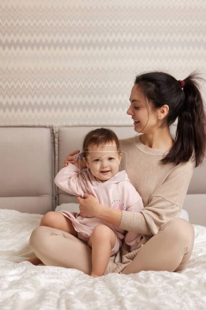 Téléchargez les photos : Belle mère peigne ses mignons cheveux de petite fille sur le lit - en image libre de droit