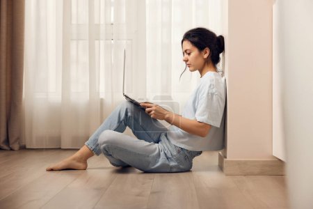 Téléchargez les photos : Femme occasionnelle assise sur le sol et travaillant sur un ordinateur portable à la maison - en image libre de droit