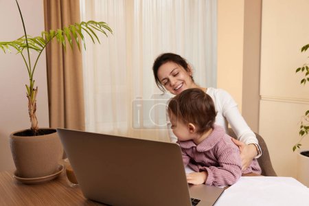 Téléchargez les photos : Femme heureuse de travail et et de jouer avec son bébé fille à la maison - en image libre de droit