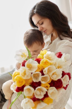 Téléchargez les photos : Mignon petit bébé fille et maman avec des tulipes de fleurs. Embrasser mère et enfant. Bonne fête des mères. - en image libre de droit