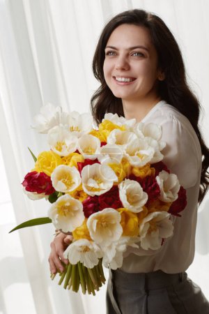 Téléchargez les photos : Belle femme dans la chemise blanche avec des tulipes de fleurs de printemps dans les mains. Journée de la femme - en image libre de droit