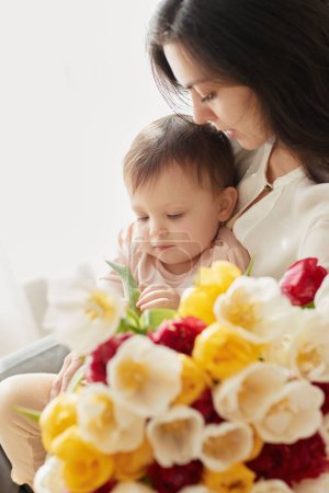 Téléchargez les photos : Mignon petit bébé fille et maman avec des tulipes de fleurs. Embrasser mère et enfant. Bonne fête des mères. - en image libre de droit