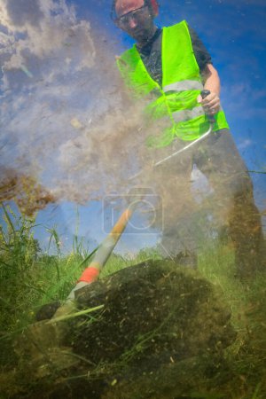 Foto de Trabajador siega hierba con cortador de hierba - Imagen libre de derechos