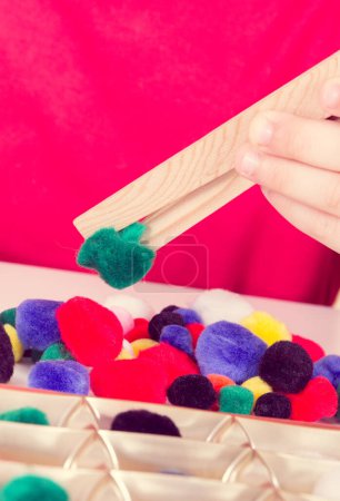 Téléchargez les photos : Preschooler jouer avec de petites pompons colorés moelleux et pinces en bois. Développement de la motricité des enfants, coordination, créativité et pensée logique - en image libre de droit