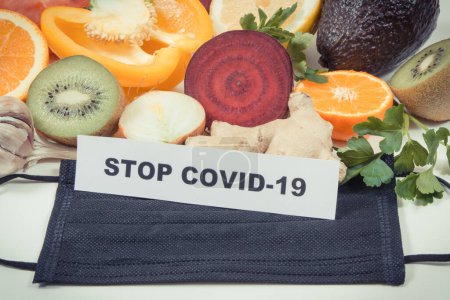 Photo for Inscription stop covid-19, fresh ripe fruits with vegetables and protective mask. Source natural healthy vitamins and minerals. Beneficial eating in times of Covid-19 - Royalty Free Image
