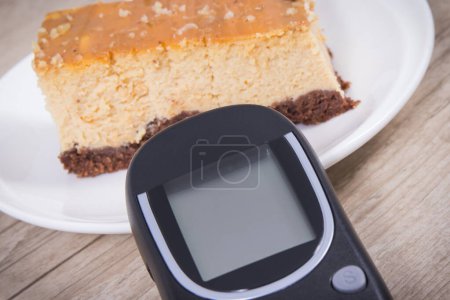 Téléchargez les photos : Glucomètre utilisé pour mesurer le niveau de sucre et gâteau au fromage sucré. Nutrition pendant le diabète concept - en image libre de droit