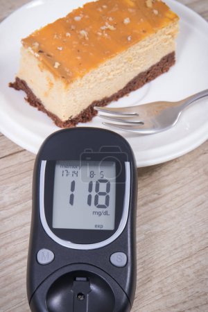 Téléchargez les photos : Glucomètre avec un résultat élevé de la mesure du taux de sucre et une portion de gâteau au fromage sucré. Nutrition pendant le diabète concept - en image libre de droit