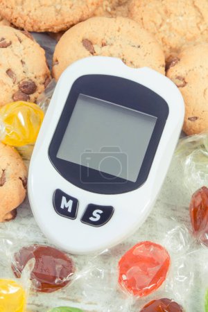 Téléchargez les photos : Glucomètre pour mesurer et vérifier le taux de sucre, les bonbons et les biscuits. Mode de vie sain, nutrition et réduction manger des bonbons pendant le diabète - en image libre de droit