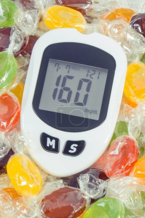 Téléchargez les photos : Compteur de glucose avec un résultat élevé de niveau de sucre et de bonbons colorés. Mode de vie sain, nutrition et réduction manger des bonbons pendant le diabète - en image libre de droit