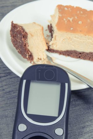 Téléchargez les photos : Glucomètre utilisé pour le contrôle du niveau de sucre et une partie de gâteau au fromage frais au four. Nutrition pendant le diabète - en image libre de droit