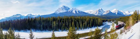 Panorama of Morant's Curve in Banff National Park with Mount Temple overlooking as red cargo train passes through. Beautiful snowy winter landscape in the Canadian rockies of Alberta.
