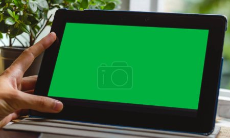 Téléchargez les photos : Gros plan d'une main tenant un comprimé avec un chromakey sur un écran, plante verte à côté - en image libre de droit
