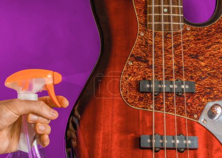 Téléchargez les photos : Hand holding a a cleaning spray before a bass guitar body, guitar care concept - en image libre de droit