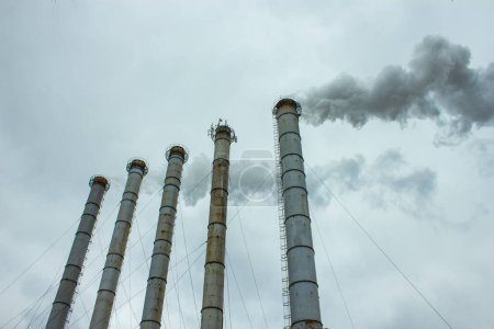 Smoke rising from steam plant stacks; gray clouds background; concept for air pollution and climate change, Kharkiv, Ukraine