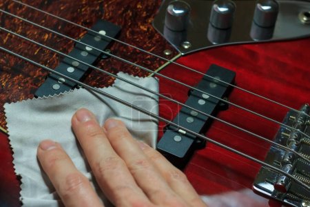 Foto de Cleaning and polishing electric bass guitar with microfiber cloth - Imagen libre de derechos