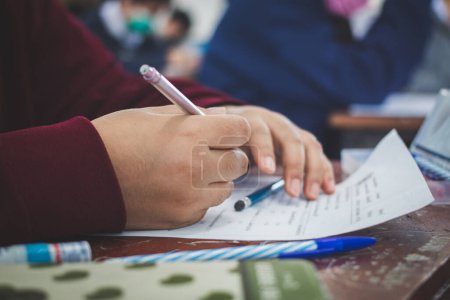 Universitätsstudent hält Stift oder Bleistift auf Papier Antwortblatt sitzt auf Stuhl Vorlesung Abschlussprüfung nimmt an Prüfungsraum oder Klassenzimmer in Uniform Student