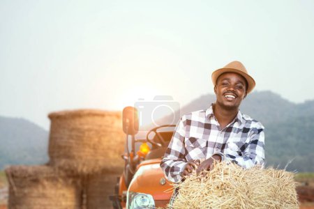 Foto de Agricultor africano frente a tractor y pajar. Agricultura o concepto de cultivo - Imagen libre de derechos