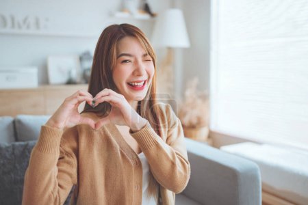 Foto de Close up of happy young asian woman smiling and showing hands sign heart shape looking at camera. Healthy heart health life insurance, love and charity, voluntary social work. - Imagen libre de derechos