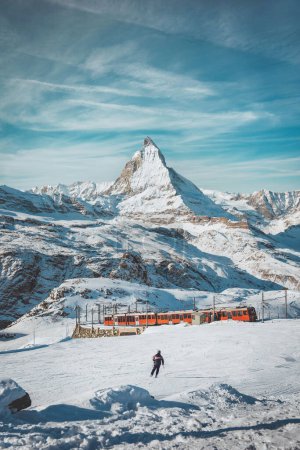 Foto de Matterhorn, Suiza, tren turístico de invierno y esquí de esquiador masculino con montaña Matterhorn en el fondo, Zermatt - Imagen libre de derechos