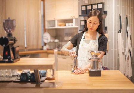 Foto de Female hand mash coffee bean in coffee grinder on wooden table. - Imagen libre de derechos