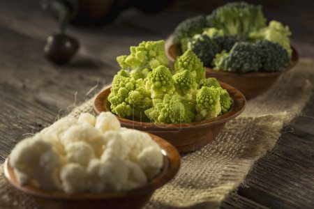 Photo for Fresh pieces of Romanesco broccoli, broccoli and cauliflower in small rustic wooden bowls. Selective focus on the Romanesco broccoli - Royalty Free Image