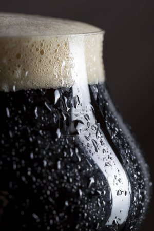 Téléchargez les photos : Gros plan d'un verre humide de bière froide foncée avec de la mousse. Concentration sélective - en image libre de droit