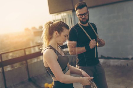 Photo for Couple standing on a building rooftop terrace, getting ready for exercising with ropes. Focus on the girl - Royalty Free Image