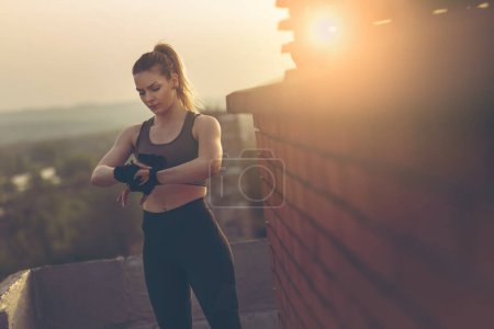 Photo for Woman wrapping hands with bandages before workout on a building rooftop terrace - Royalty Free Image