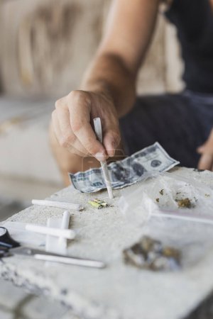 Foto de Detalle de las manos masculinas enrollando una articulación con papel de liar y brotes de cannabis en el fondo - Imagen libre de derechos