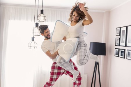 Foto de Feliz pareja amorosa divirtiéndose mientras tiene una pelea de almohadas y saltar en la cama - Imagen libre de derechos
