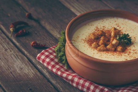 Photo for Bowl of cauliflower cream soup decorated with grounded red pepper and some croutons on a rustic wooden table. Selective focus on the croutons - Royalty Free Image