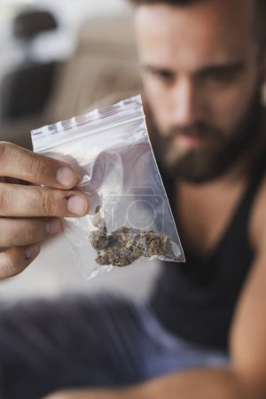 Foto de Traficante de drogas vendiendo heroína, sentado en el sofá y ofreciendo una dosis de heroína en una bolsa al comprador - Imagen libre de derechos