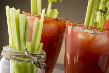Photo for Bloody Mary cocktail with vodka, lemon and tomato juice, tabasco sauce and ice cubes decorated with celery leaves. Focus on the right glass - Royalty Free Image
